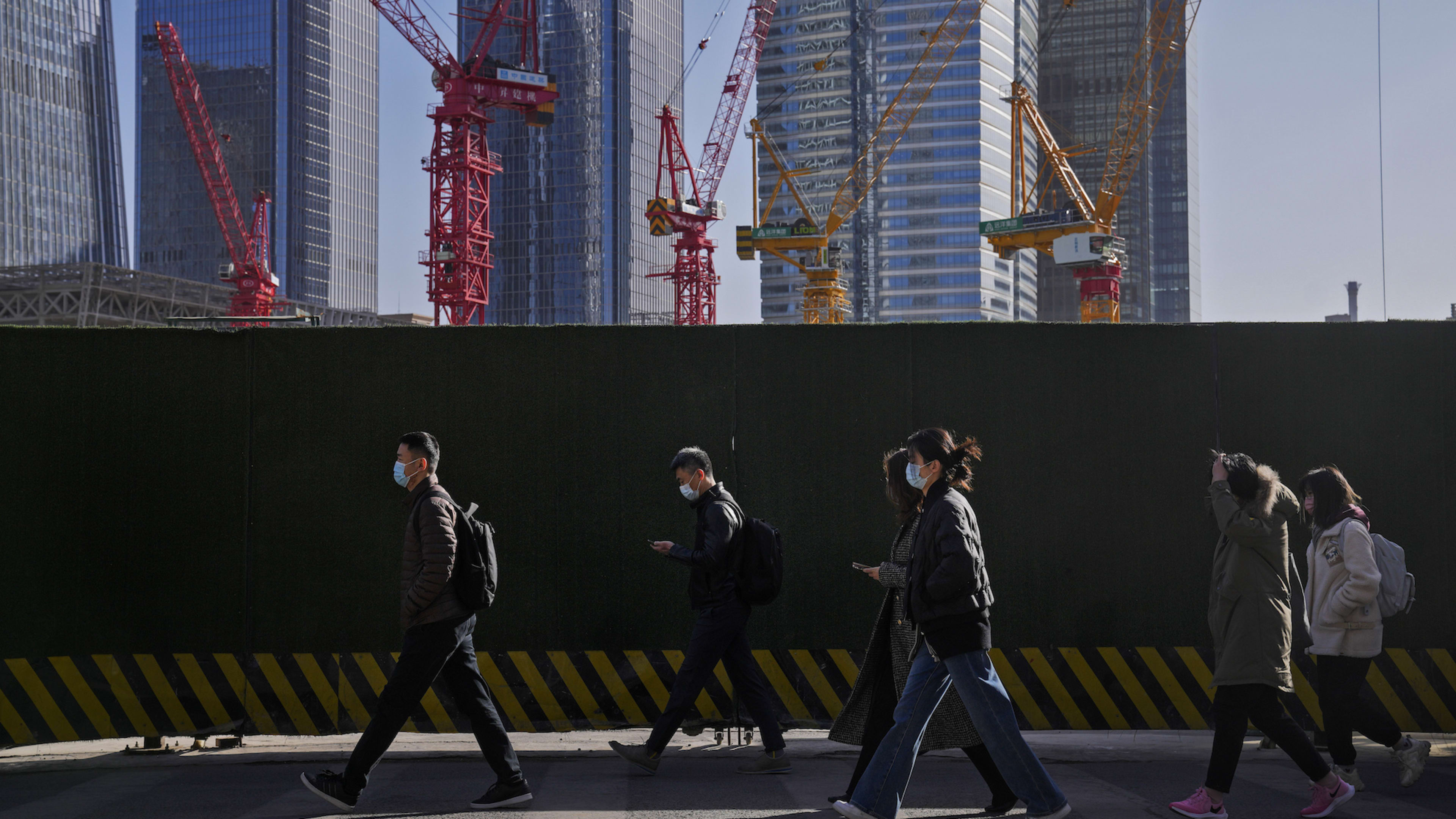 People wearing face masks walk by construction cranes near the office buildings at the central business district in Beijing,