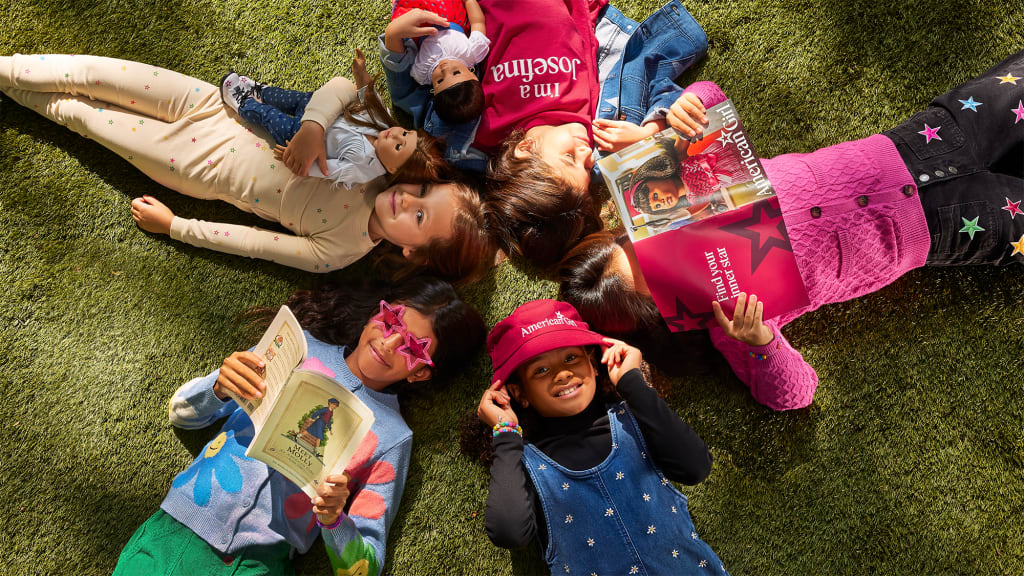 A photo of five girls lying down on the grass and reading books in a circle. 