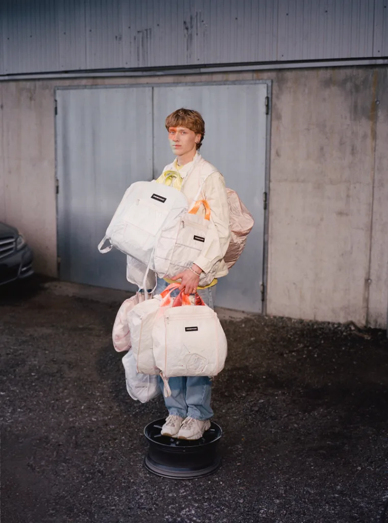 A full-length photo of a model from 3/4 perspective carrying seven Freitag bags.
