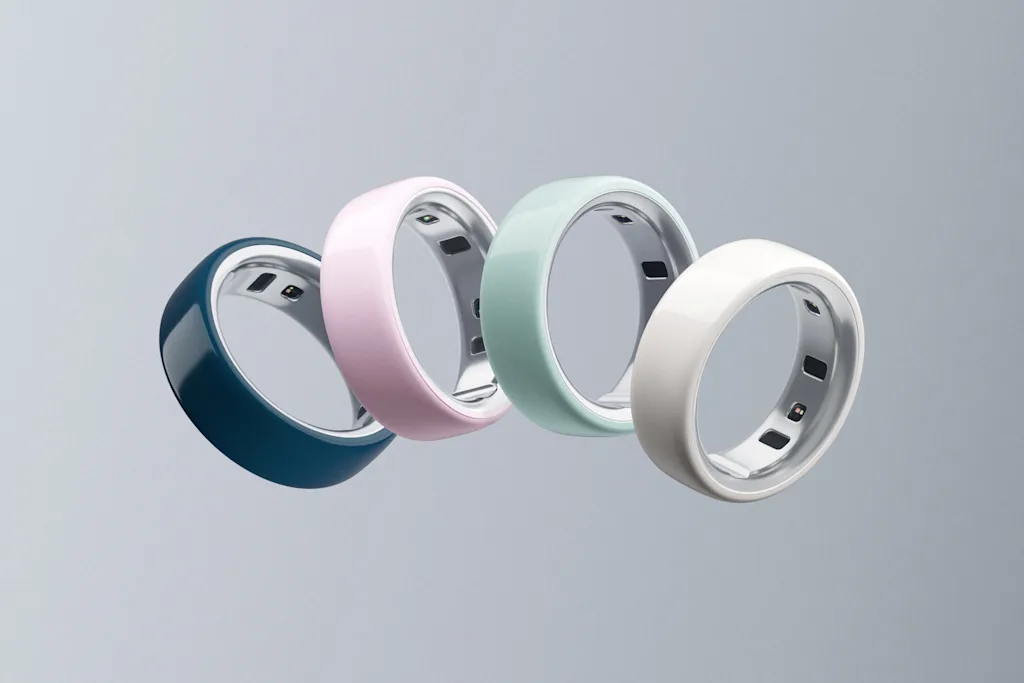 Cuatro anillos Oura, uno en cada uno de los nuevos colores, flotan en un arco frente a un fondo gris degradado.
