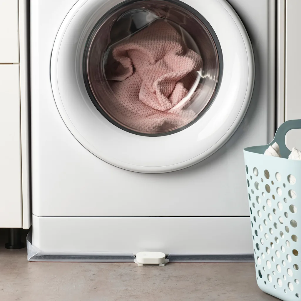 A water sensor within Ikea's smart home range sits on the floor in front of a washing machine.