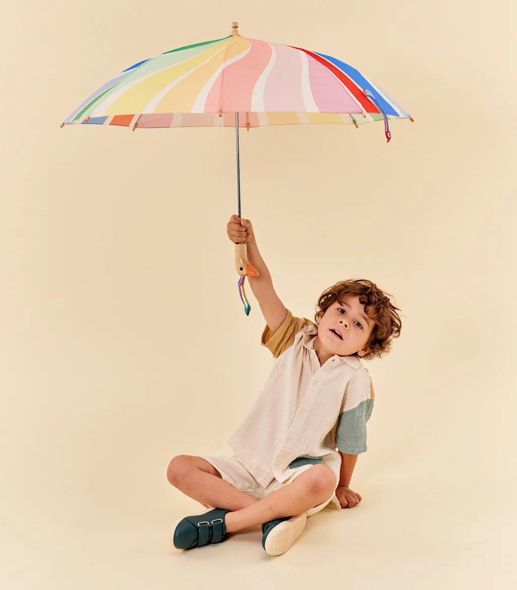 A child holding a colorful striped umbrella, which has a wooden handle carved in the shape of a ducks head .