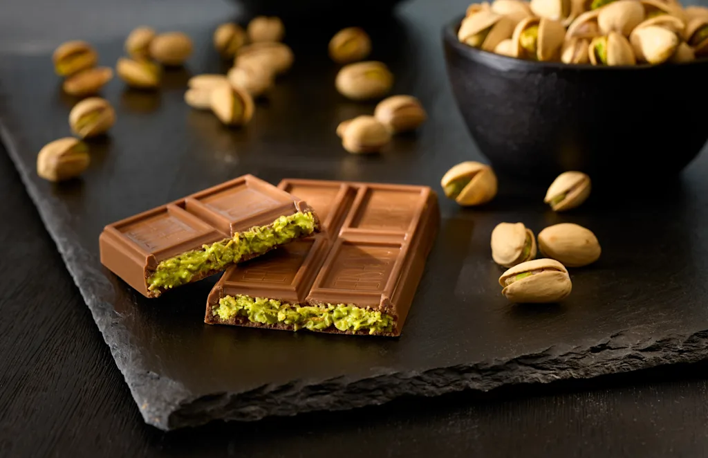 A product photo of an unwrapped Hershey's Dubai chocolate bar next to a bowl of pistachios.