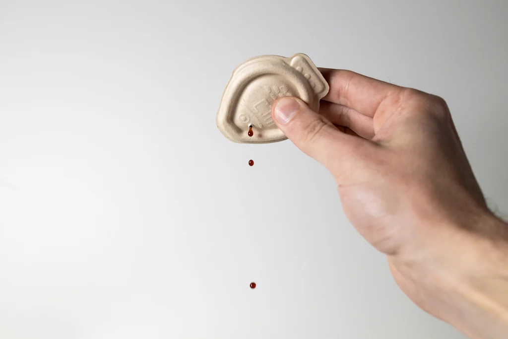 A hand dispenses soy sauce from a Holy Carp soy sauce dropper.