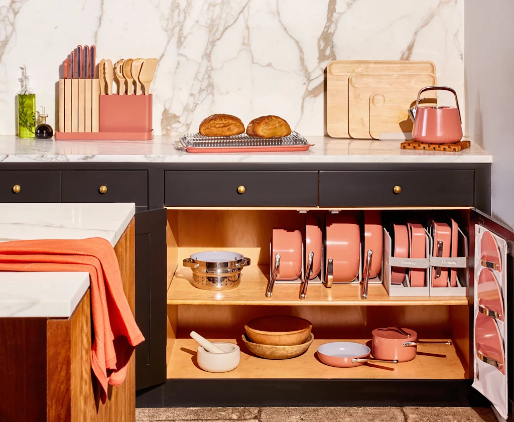 A high flash photo of an open kitchen cabinet with Caraway pans inside.