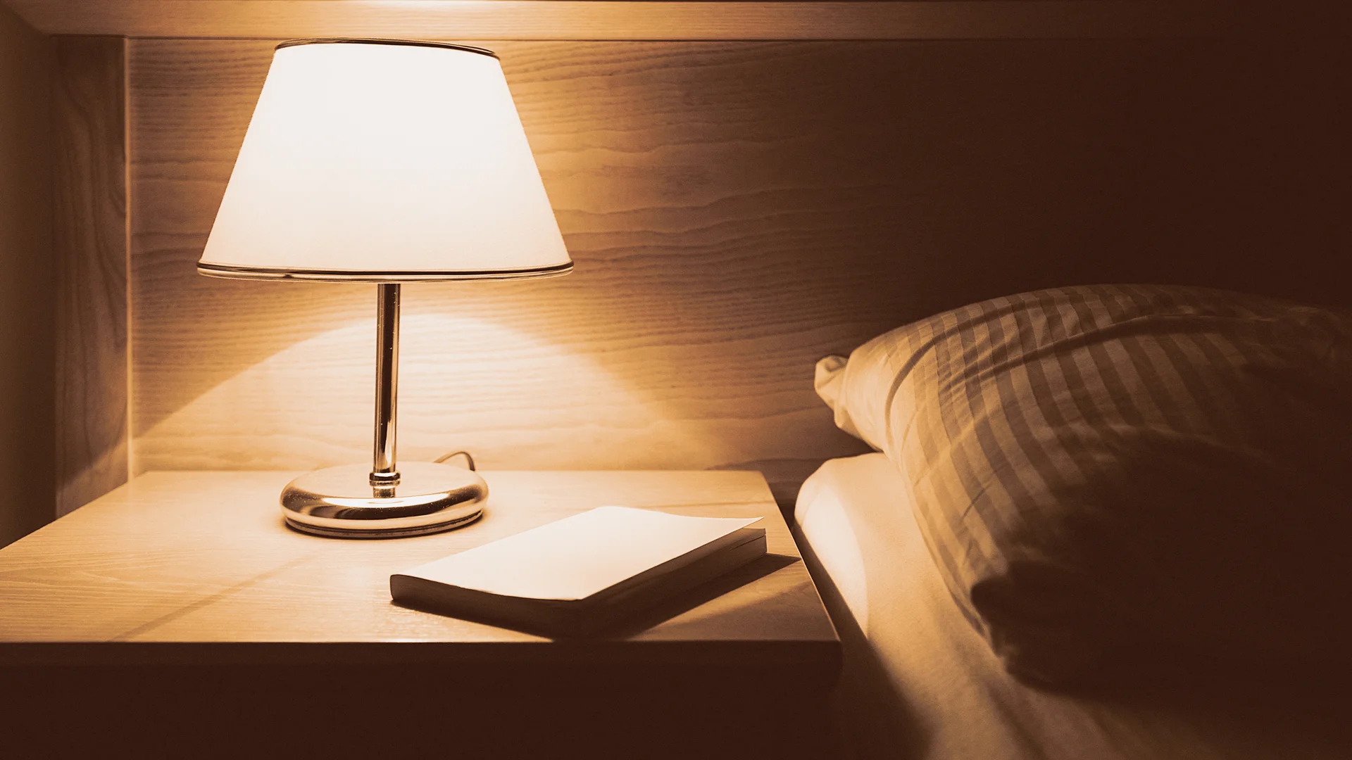 A person setting up their bedroom for optimal sleep, including adjusting the thermostat, dimming the lights, and preparing a dream journal
